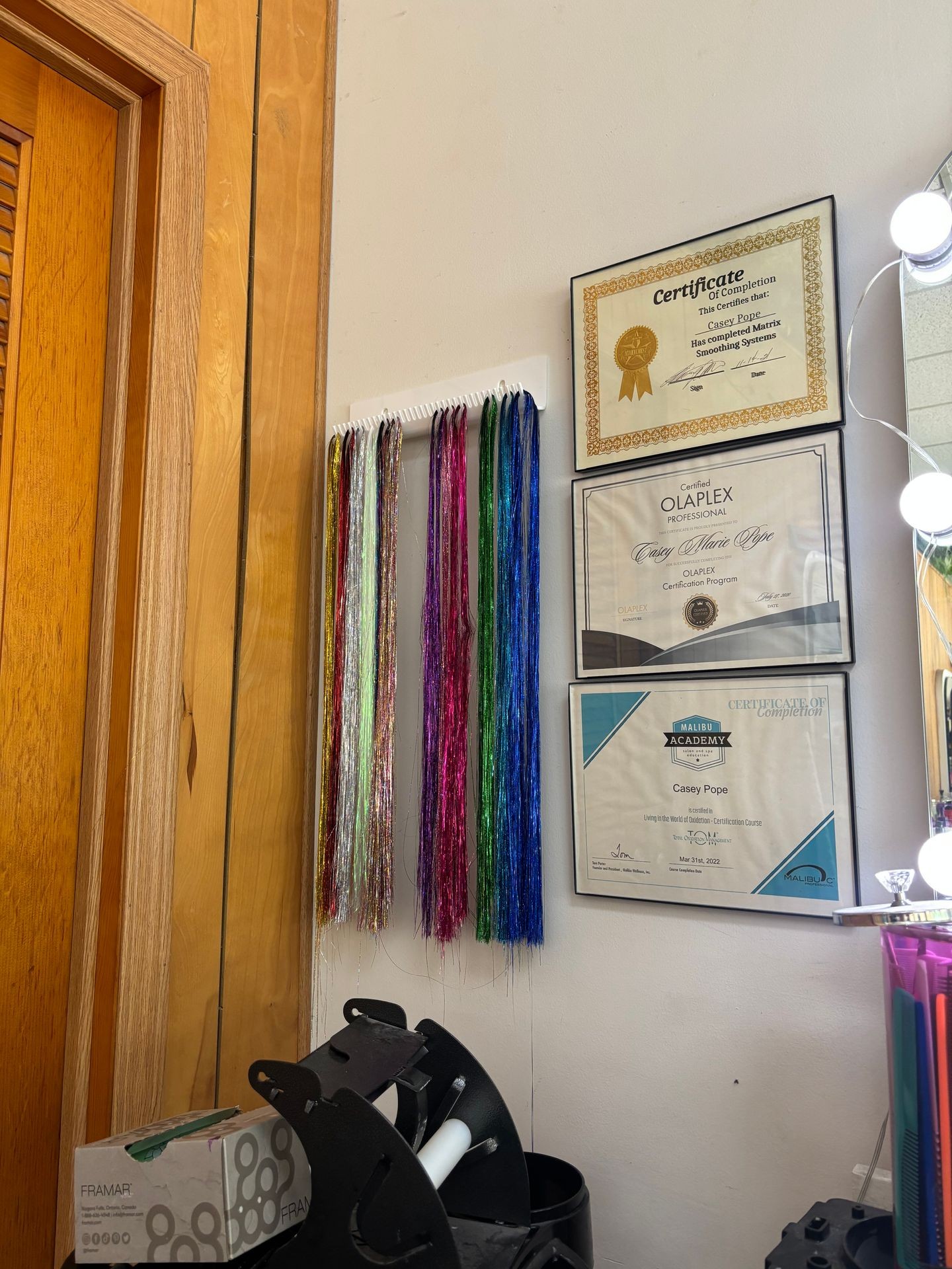 Wall display with colorful hair extensions and framed certificates in a hair salon.